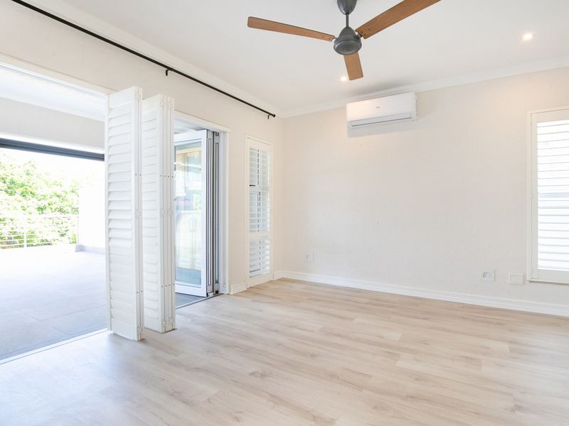 Bright and spacious living area featuring light laminate flooring, a ceiling fan, air conditioning, and bi-fold doors opening onto a private balcony.