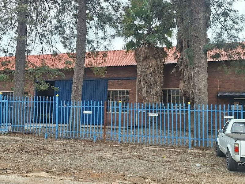 Commercial property featuring a brick facade, corrugated metal roof, and secure steel perimeter fencing with industrial sliding access doors.