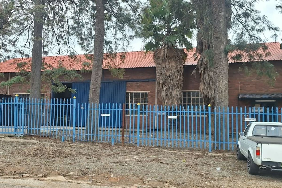 Commercial property featuring a brick facade, corrugated metal roof, and secure steel perimeter fencing with industrial sliding access doors.
