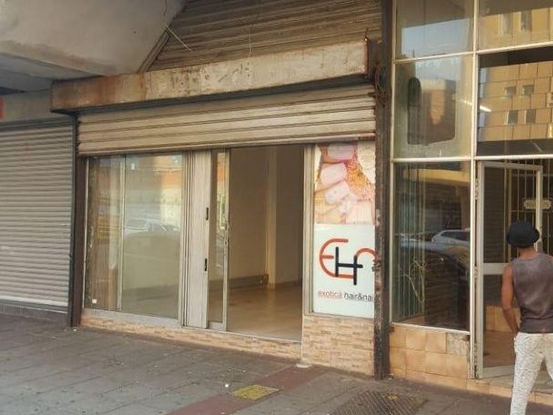 Street-level commercial storefront featuring a glass entrance and metal roller shutter, located within a multi-story building.