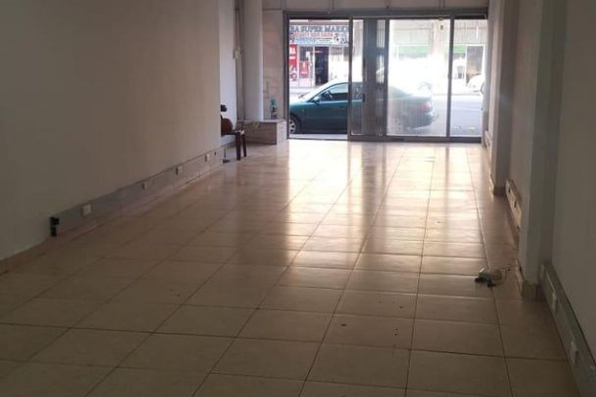 An empty commercial open-plan space featuring tiled flooring, a suspended ceiling with recessed lighting, and a large sliding glass entrance door.