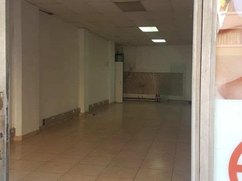 An empty commercial open-plan space featuring tiled flooring, a suspended ceiling with recessed lighting, and a tiled rear splashback area.
