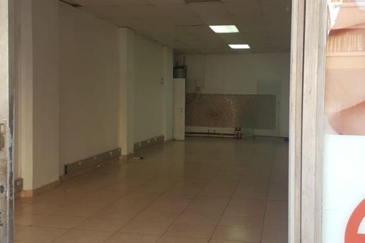 An empty commercial open-plan space featuring tiled flooring, a suspended ceiling with recessed lighting, and a tiled rear splashback area.