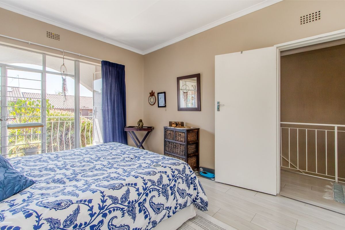A bedroom featuring laminate flooring, cove cornicing, and a sliding glass door providing access to a balcony with metal security gate.