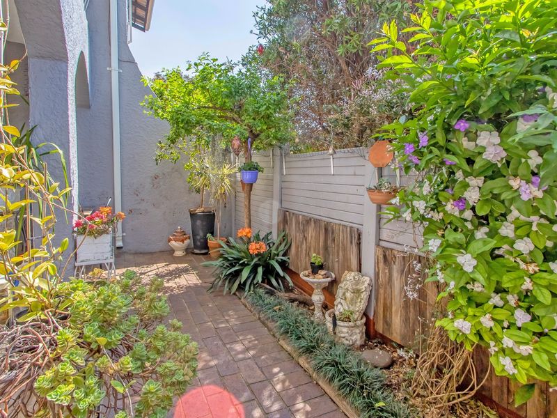 A private rear garden area featuring paved flooring and a timber boundary fence, surrounded by established greenery and garden beds.