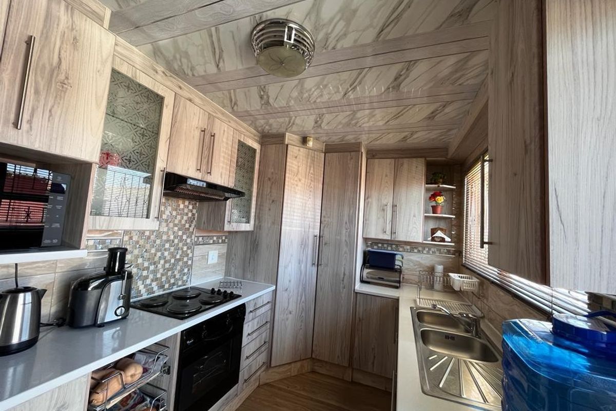 A functional kitchen featuring wood-grain cabinetry, mosaic tile backsplash, integrated electric hob and oven, and a double bowl stainless steel sink.