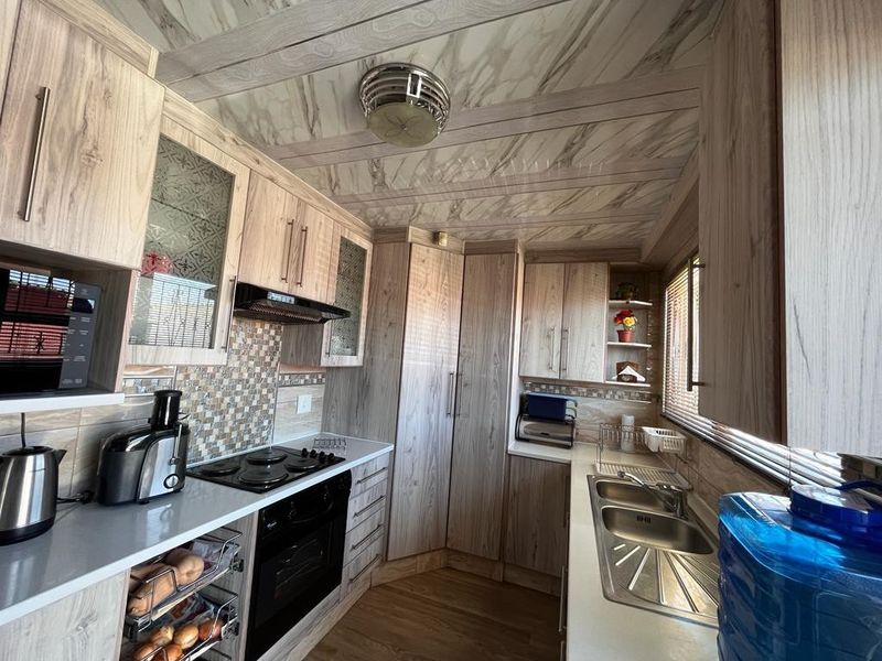 A functional kitchen featuring wood-grain cabinetry, mosaic tile backsplash, integrated electric hob and oven, and a double bowl stainless steel sink.