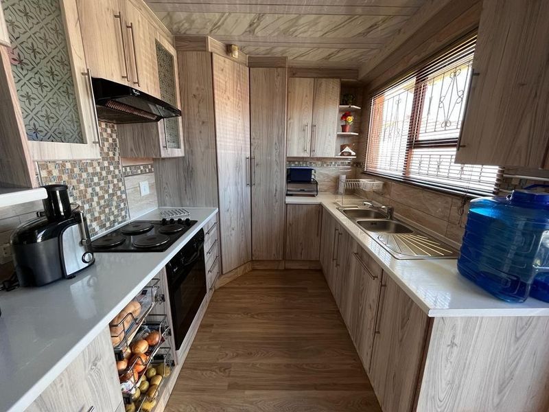 A functional kitchen featuring wood-look cabinetry, laminate countertops, a built-in electric hob, oven, extractor fan, and a stainless steel double sink.