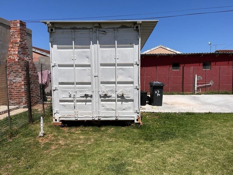 Rear yard area featuring a metal shipping container, a brick chimney structure, and a concrete paved section enclosed by wire fencing.