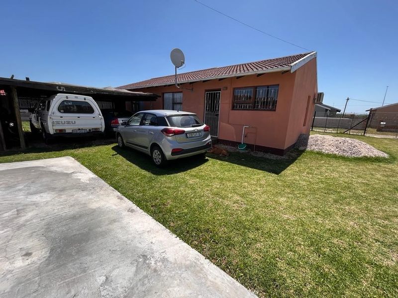Rear view of the property featuring a carport, concrete driveway, and a lawn area with a tiled roof structure.