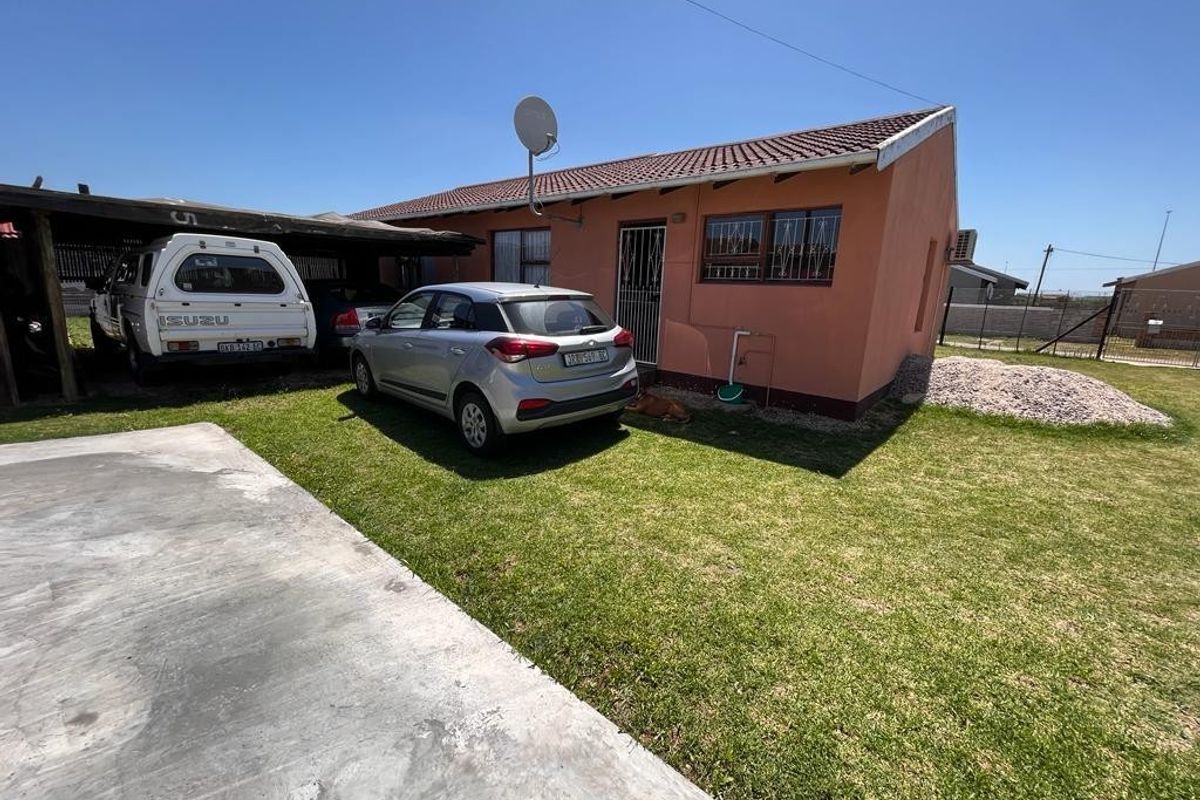 Rear view of the property featuring a carport, concrete driveway, and a lawn area with a tiled roof structure.