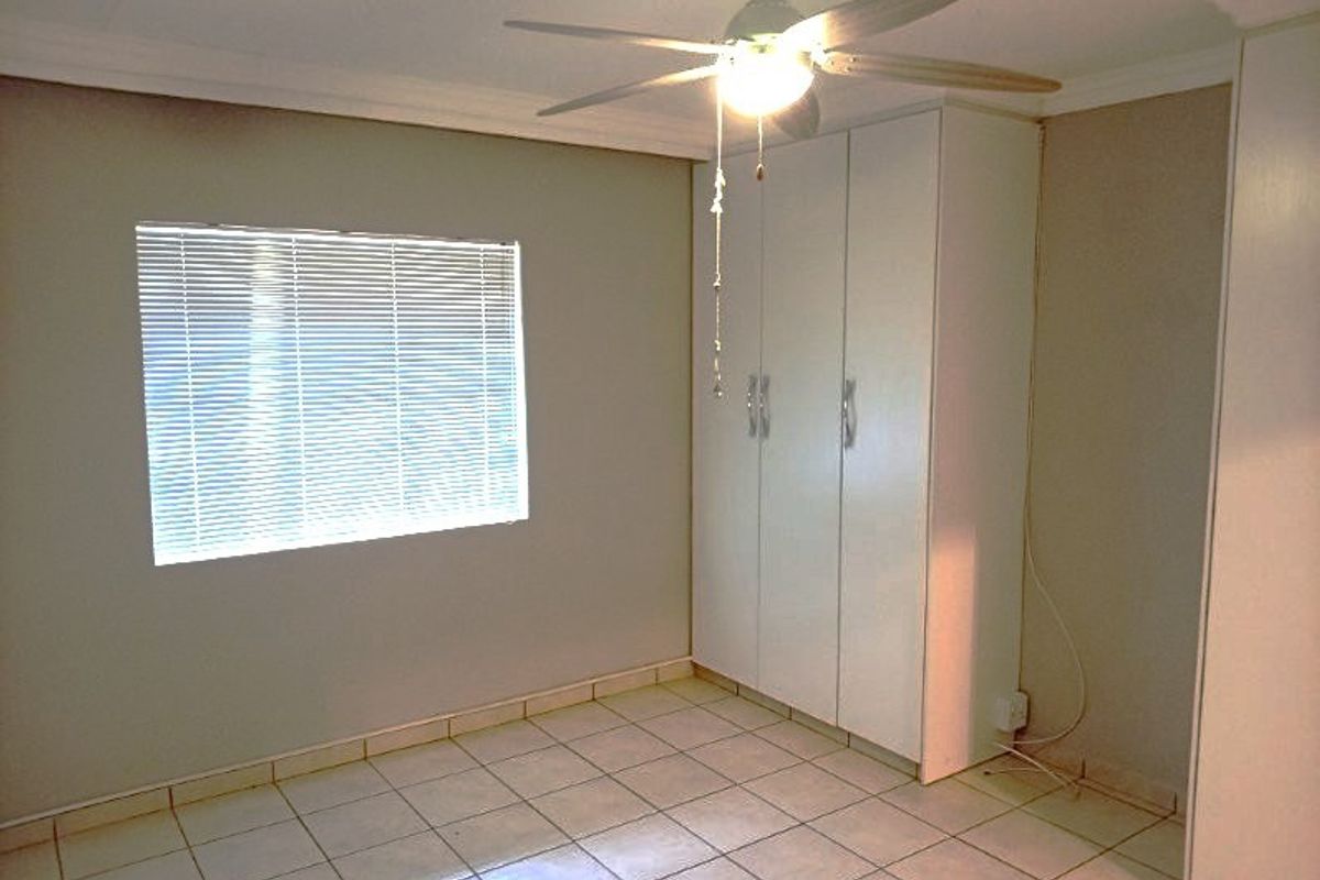A clean, empty bedroom featuring tiled flooring, built-in cupboards, a ceiling fan, and venetian blinds on the window.