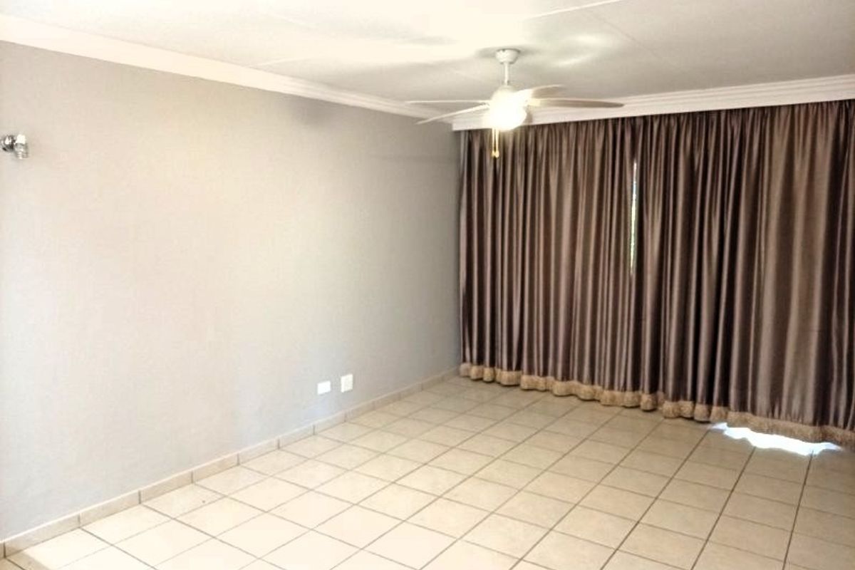 A spacious, empty living area featuring neutral tiled flooring, a ceiling fan, and coved cornicing, providing a blank canvas for personalization.