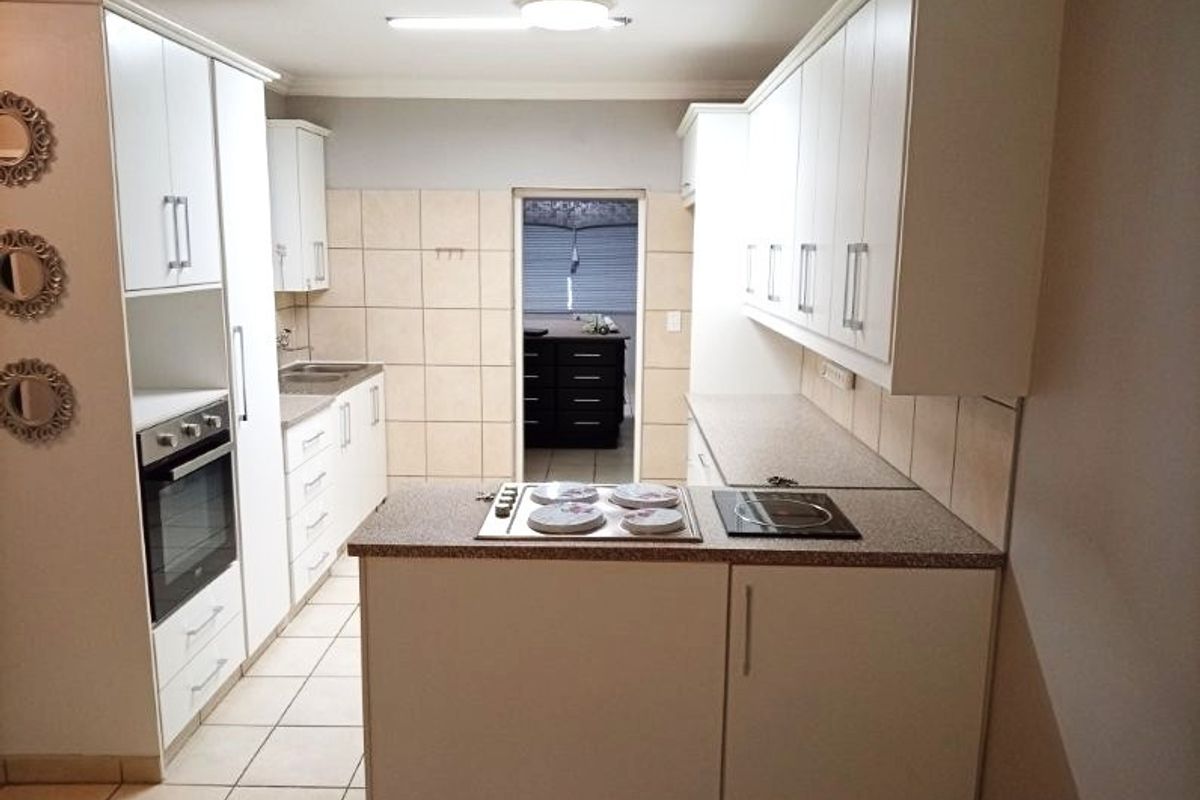 A functional kitchen featuring white cabinetry, laminate countertops, a built-in oven, and an electric hob with tiled splashbacks and ceramic flooring.