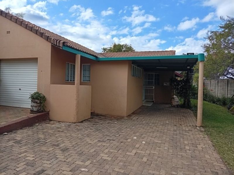 Front exterior view of the retirement unit featuring a paved driveway, covered carport, and a single garage with a roller door.