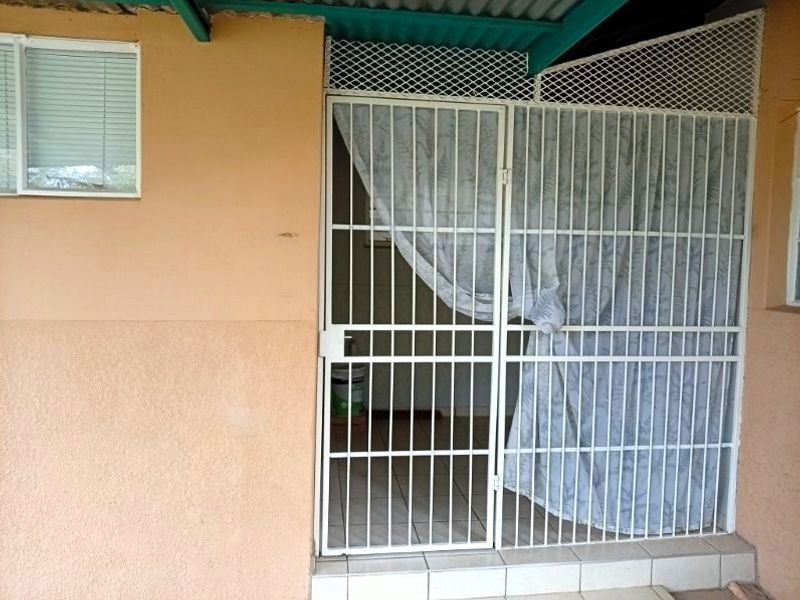 A covered patio area featuring tiled flooring, a security gate, and a lattice screen, providing a functional outdoor space.