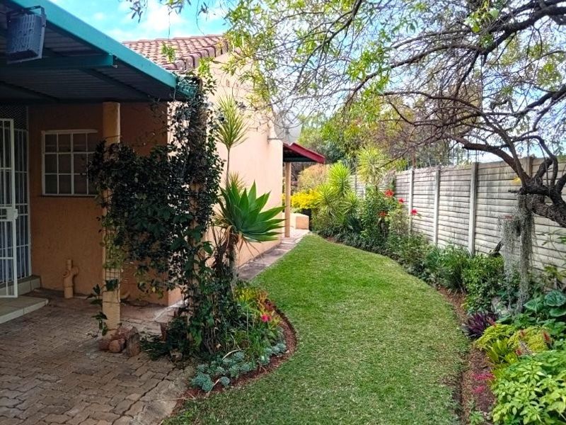 A well-maintained rear garden featuring a paved patio area, covered veranda, and established landscaping enclosed by a precast concrete boundary wall.