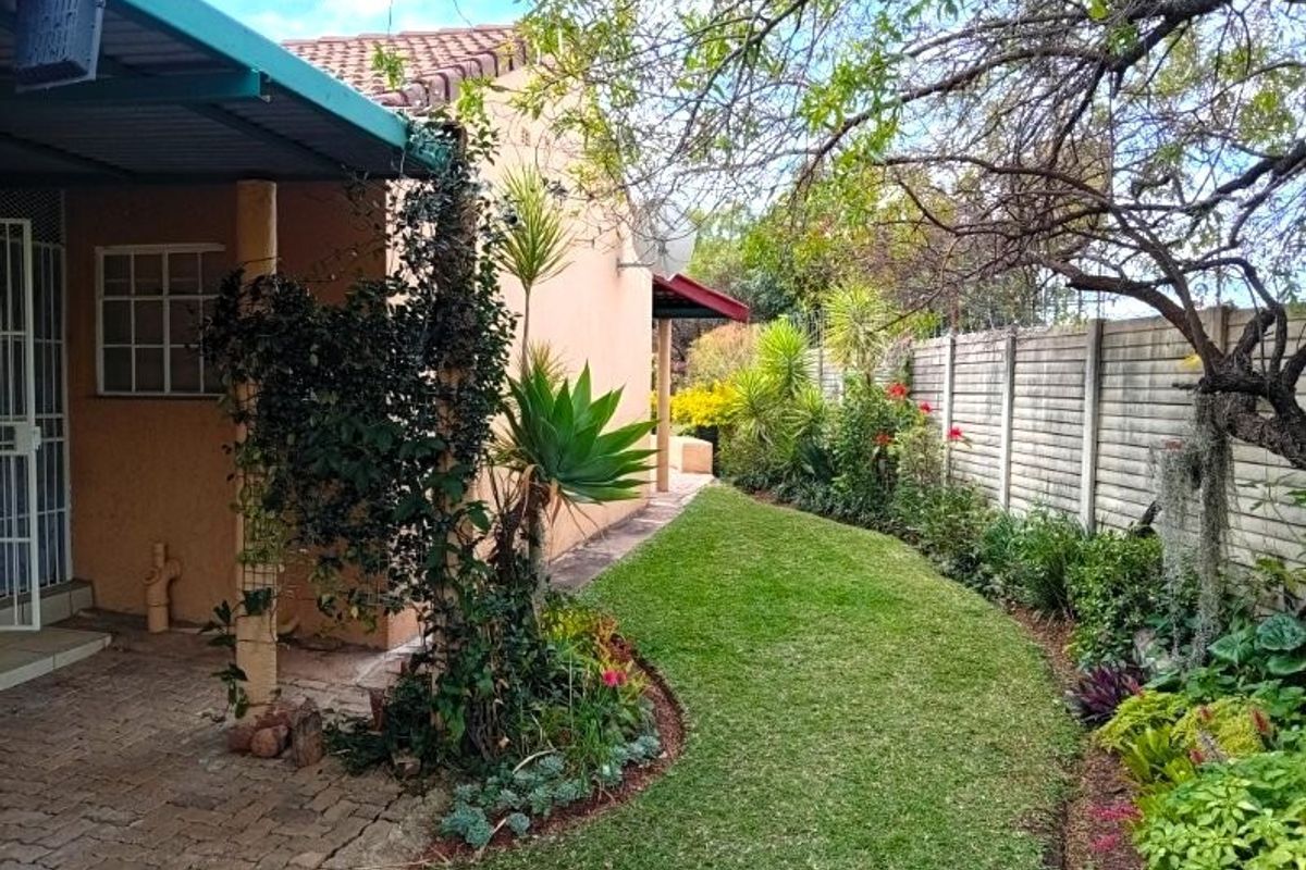 A well-maintained rear garden featuring a paved patio area, covered veranda, and established landscaping enclosed by a precast concrete boundary wall.