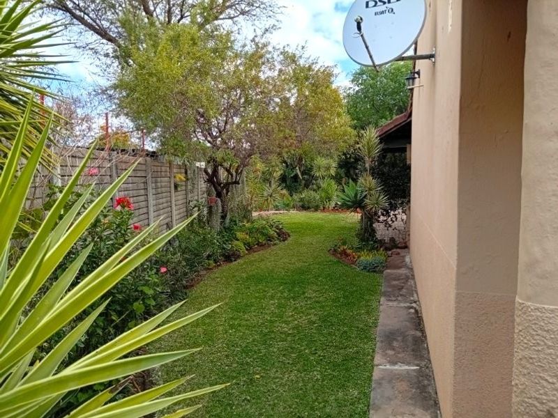 A well-maintained rear garden area featuring a lush lawn, established garden beds, and a concrete pathway running alongside the building exterior.