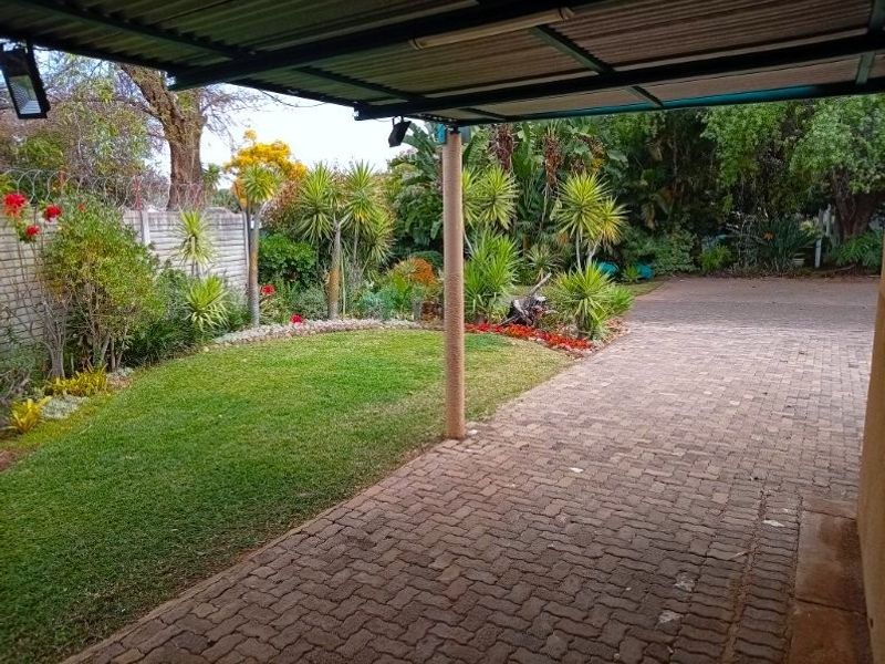 A well-maintained front exterior featuring a paved driveway, covered carport, and a landscaped garden with a secure perimeter wall.