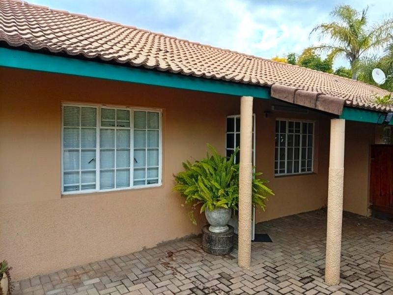 A rear exterior view of the retirement unit featuring a paved patio area, tiled roof, and established garden surroundings.