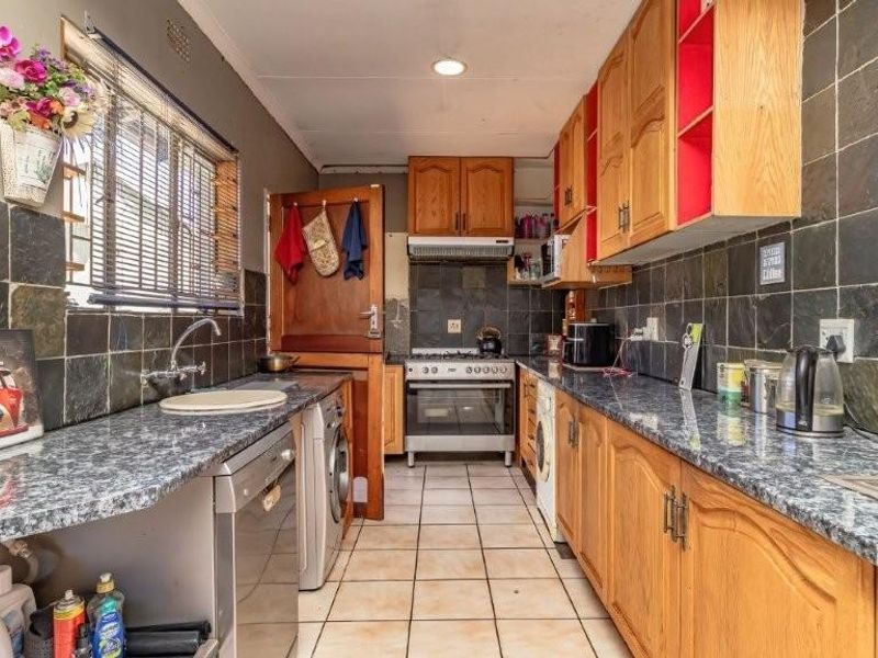 A functional galley-style kitchen featuring wooden cabinetry, granite-look countertops, slate tile backsplash, and integrated space for under-counter appliances.