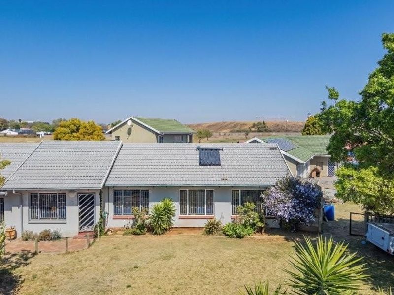 Rear view of the property featuring a tiled roof with solar water heating, security bars on windows, and a paved patio area overlooking the garden.