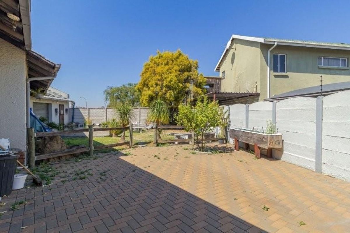 A rear exterior view featuring a paved patio area, enclosed by precast concrete boundary walls with electric fencing and a timber post and rail fence.