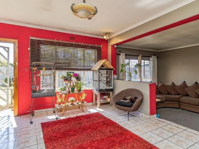 Open plan living area featuring tiled flooring, a security gate entrance, and a semi-partitioned lounge space with neutral and bold wall finishes.