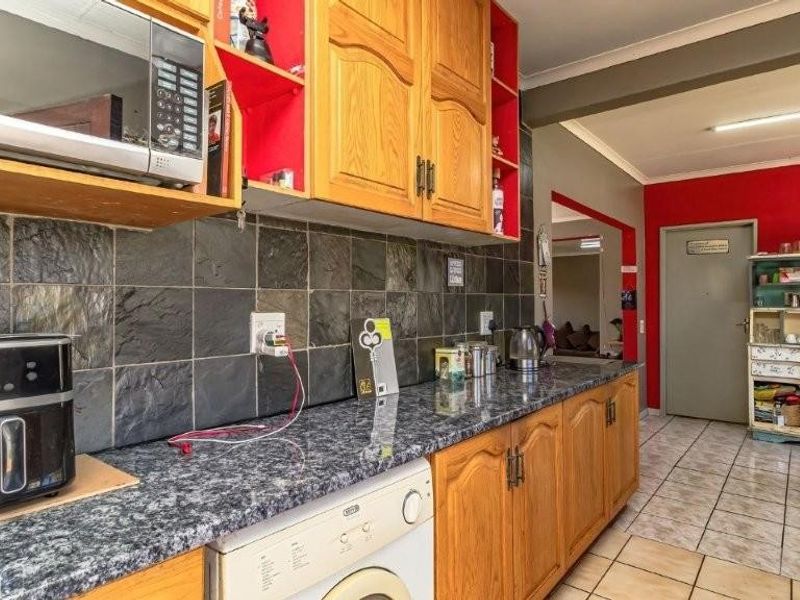 A functional kitchen featuring wooden cabinetry, slate tile backsplash, and stone-look countertops, with an adjacent tiled dining area.
