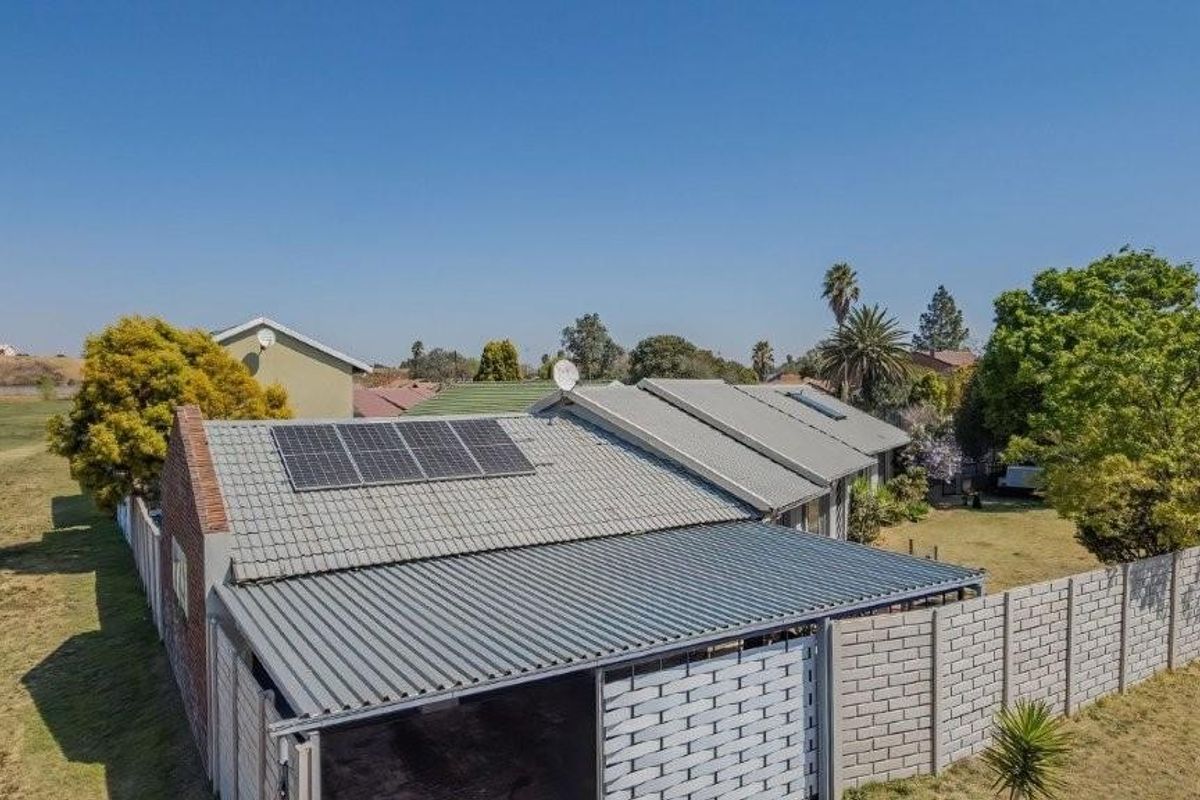 Aerial view of the property featuring a tiled roof with solar panels, a large corrugated metal carport, and a secure precast concrete boundary wall.