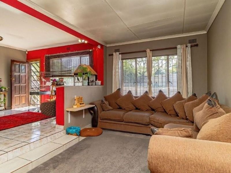 Open plan living area featuring a split-level design with tiled and carpeted flooring, large windows with security bars, and a distinct red accent wall.