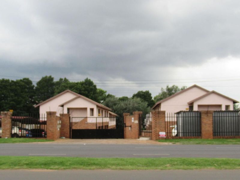 Front exterior view of an apartment complex featuring brick boundary walls, metal security gates, and covered parking areas.