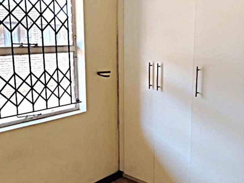 A bedroom featuring built-in cupboards and a window fitted with a security gate.
