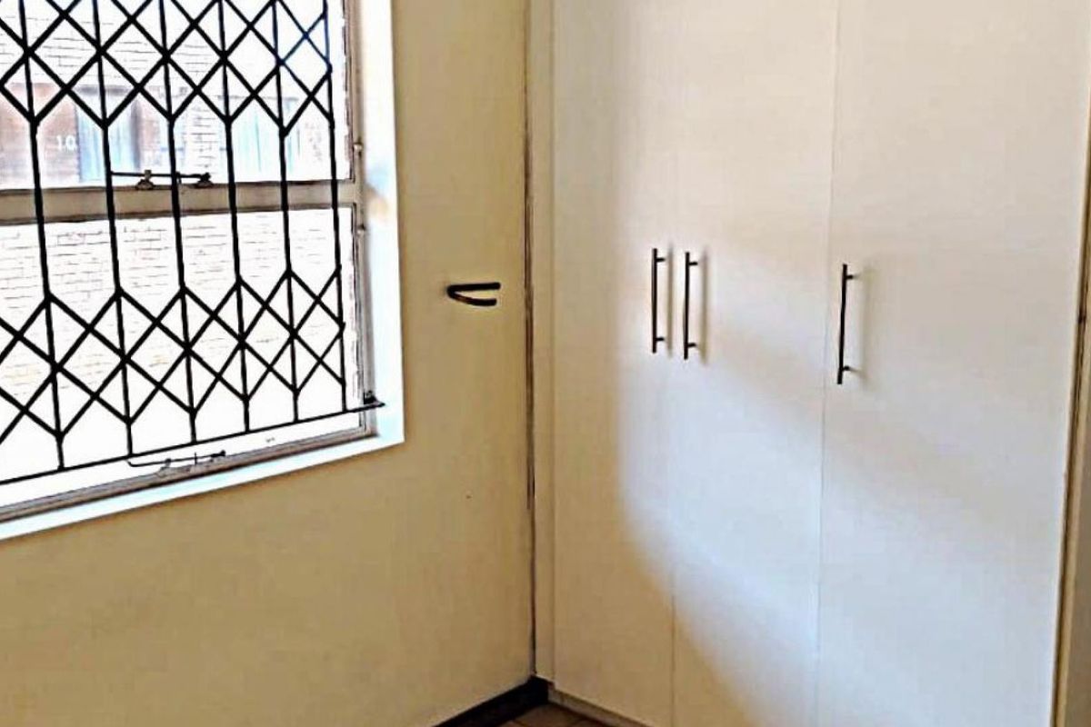 A bedroom featuring built-in cupboards and a window fitted with a security gate.