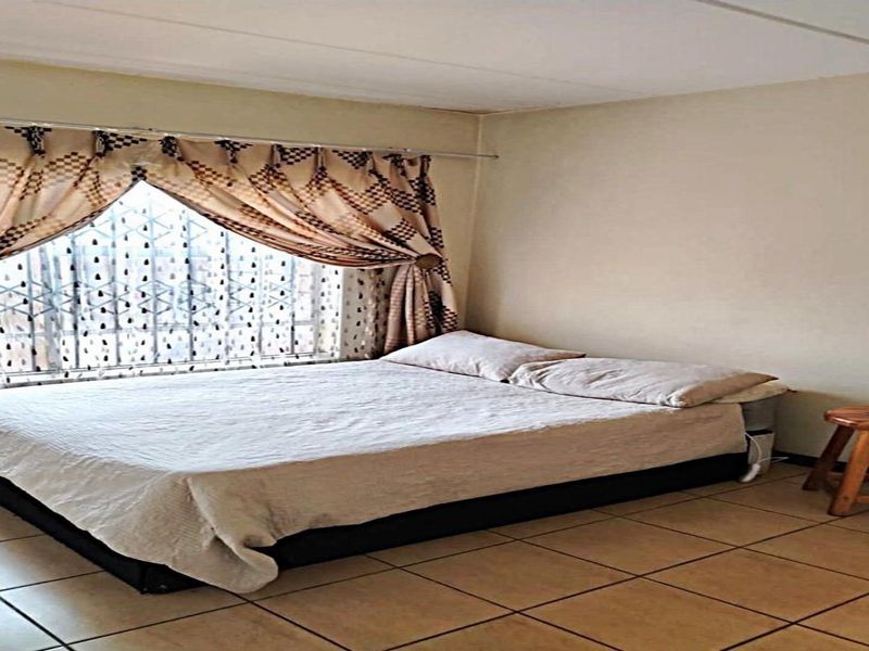 A bedroom featuring tiled flooring and security bars on the window, requiring some maintenance to the ceiling.