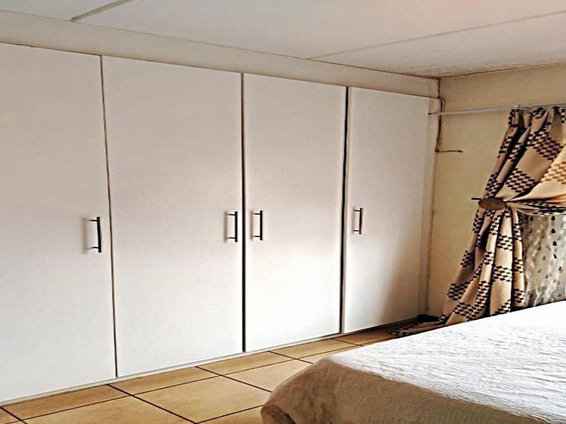 Bedroom featuring built-in cupboards and tiled flooring, showing signs of ceiling wear and water staining.