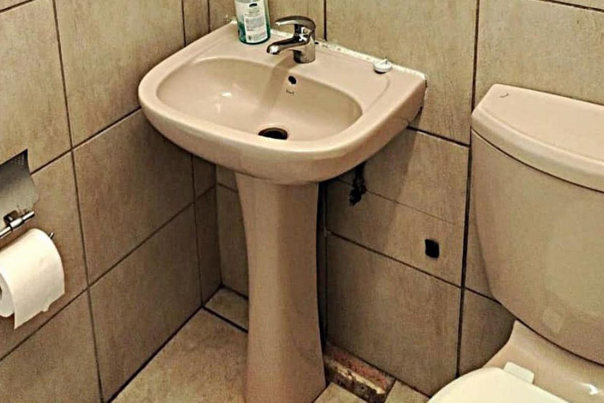 A compact bathroom featuring a pedestal basin, ceramic toilet, and neutral wall tiling. The space requires minor repairs to floor tiles and plumbing fixtures.