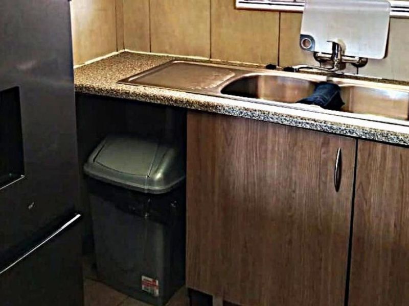 A compact kitchen area featuring a stainless steel sink, laminate countertops, and wood-finish cabinetry with a tiled backsplash.