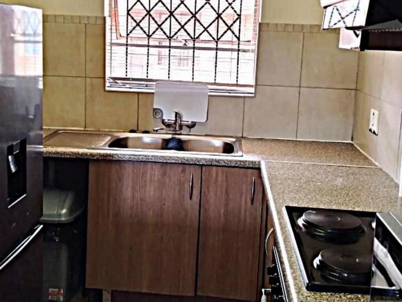 A functional kitchen featuring granite countertops, built-in wooden cabinetry, a double sink, and an integrated electric hob with an extractor fan.