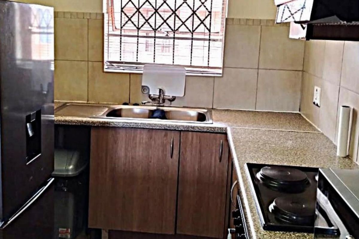 A functional kitchen featuring granite countertops, built-in wooden cabinetry, a double sink, and an integrated electric hob with an extractor fan.