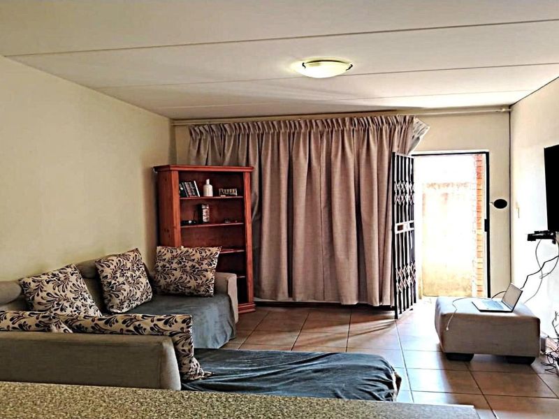 A functional living room featuring tiled flooring, a ceiling light fixture, and direct access to an outdoor area through a security gate.