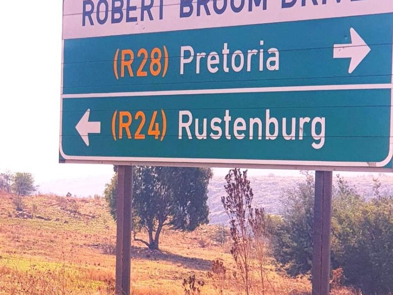 A road sign indicating directions to Pretoria and Rustenburg, situated on a vacant residential plot.