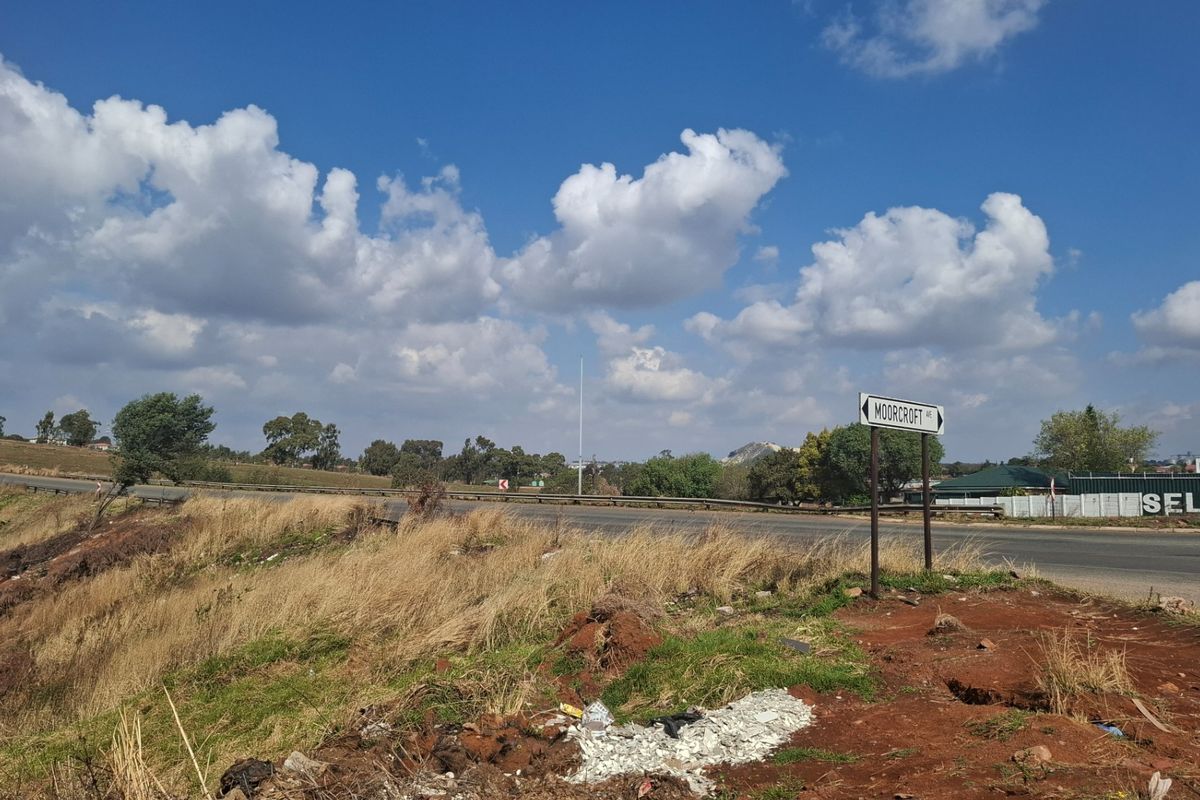 A view of the street frontage and surrounding landscape, showing the road access and local signage near the vacant land.
