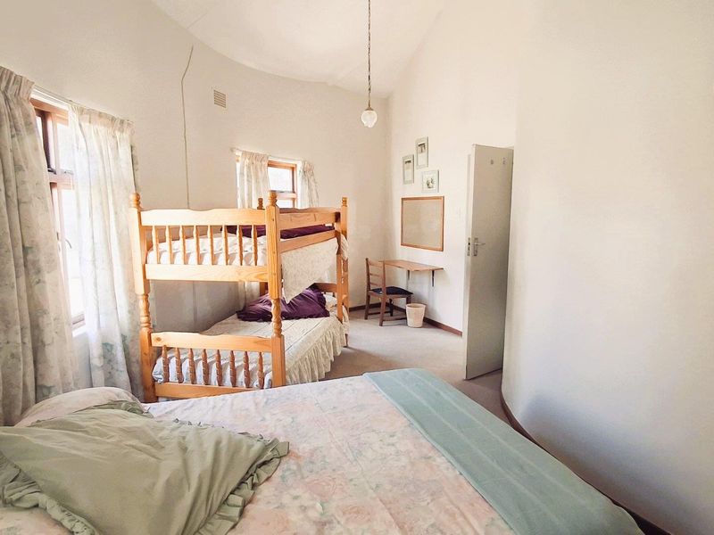 A spacious bedroom featuring a unique curved wall, vaulted ceiling, and a built-in desk area, offering a functional layout with natural light.