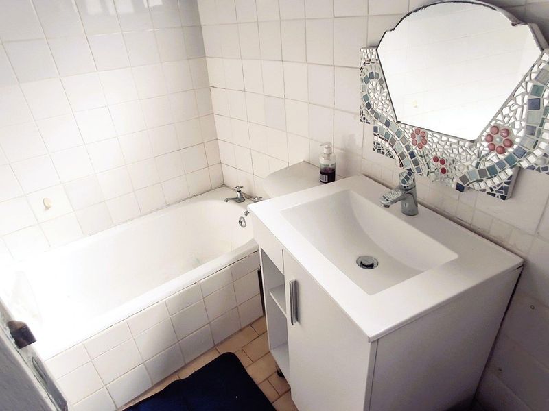 A functional bathroom featuring a built-in bathtub, a modern white vanity cabinet with basin, and tiled wall finishes.