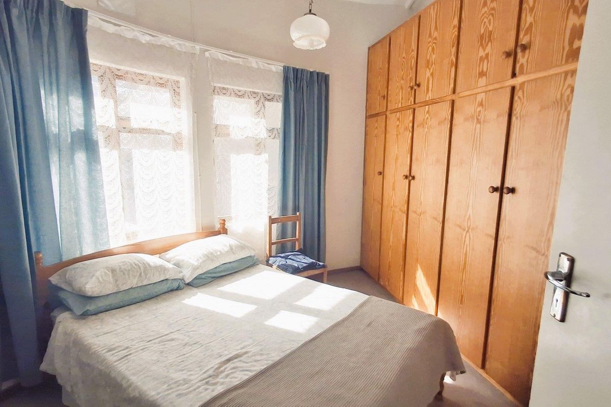 A bedroom featuring floor-to-ceiling built-in wooden cupboards and natural light from the windows.