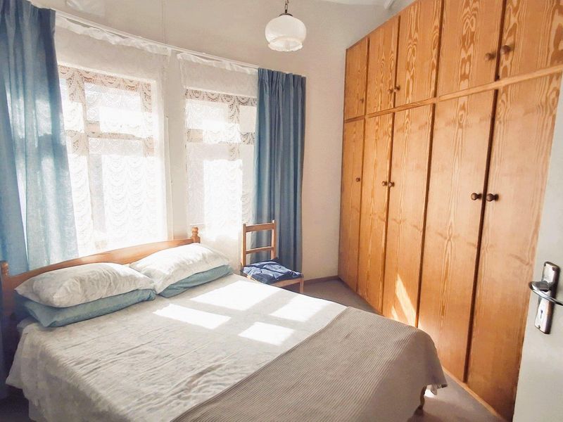 A bedroom featuring floor-to-ceiling built-in wooden cupboards and natural light from the windows.