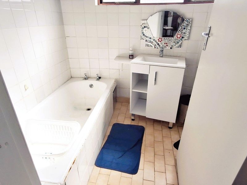 A compact bathroom featuring a built-in bathtub, a vanity cabinet with a basin, and tiled surfaces throughout.