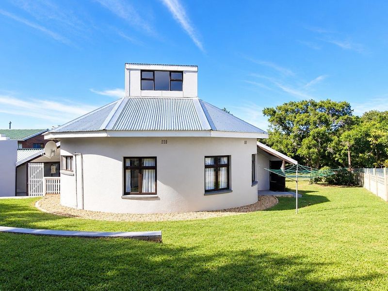 Rear view of a unique circular house featuring a corrugated metal roof, clerestory windows, and a well-maintained lawn with boundary walling.